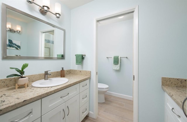 full bath featuring vanity, baseboards, wood finished floors, and toilet