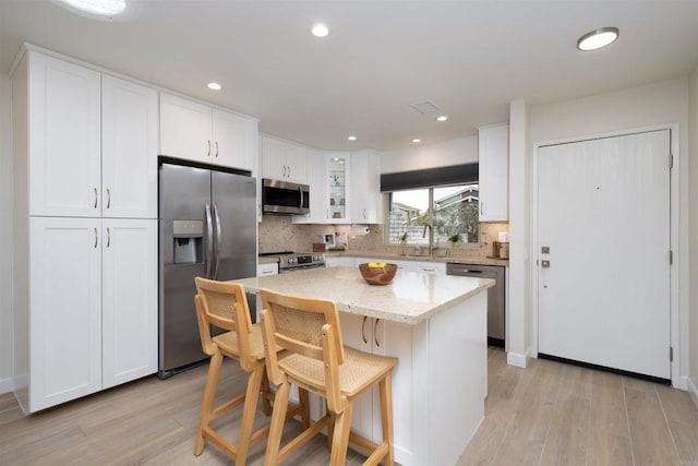 kitchen featuring decorative backsplash, stainless steel appliances, white cabinetry, and light wood-style flooring