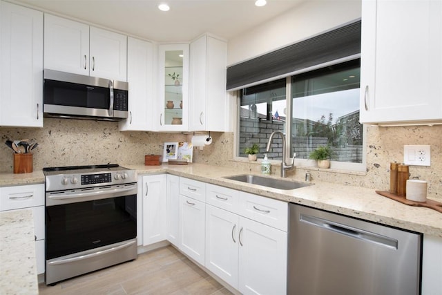 kitchen featuring a sink, light stone counters, stainless steel appliances, and white cabinetry