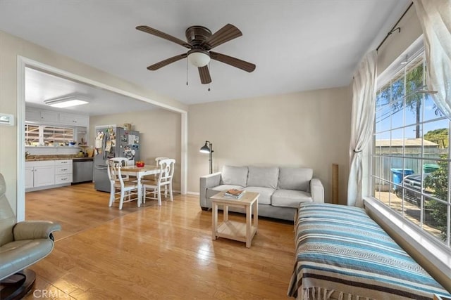living area with light wood-style floors, baseboards, and ceiling fan