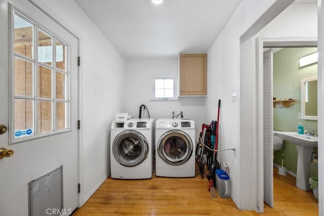 washroom featuring a sink, light wood finished floors, cabinet space, and washing machine and clothes dryer