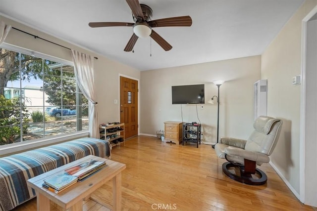 living area with baseboards, light wood finished floors, and ceiling fan