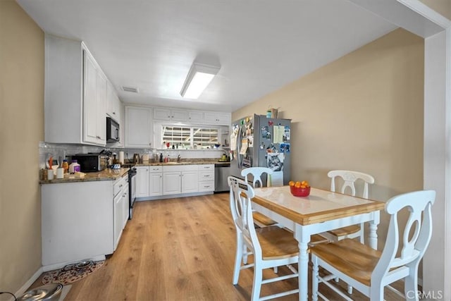 kitchen featuring appliances with stainless steel finishes, white cabinetry, light wood-type flooring, tasteful backsplash, and visible vents