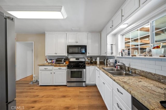 kitchen featuring black microwave, a sink, white cabinetry, decorative backsplash, and gas range