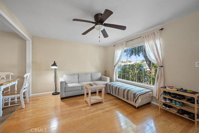 living area featuring baseboards, light wood-style flooring, and ceiling fan