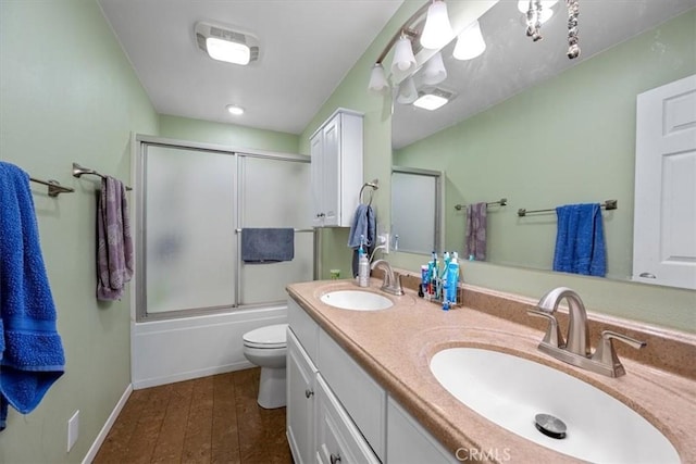 bathroom with double vanity, toilet, combined bath / shower with glass door, and a sink
