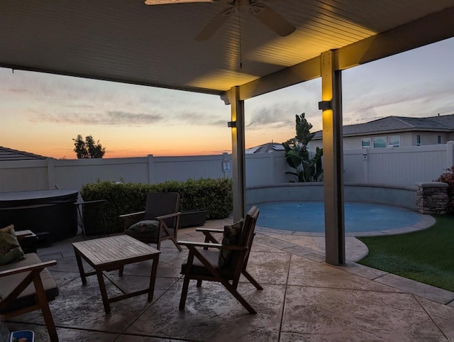 patio terrace at dusk featuring a hot tub, a fenced backyard, and a ceiling fan