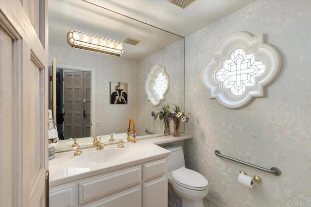 half bath featuring vanity, wallpapered walls, toilet, and visible vents