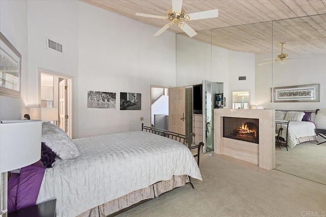 carpeted bedroom with high vaulted ceiling, wood ceiling, a warm lit fireplace, and visible vents