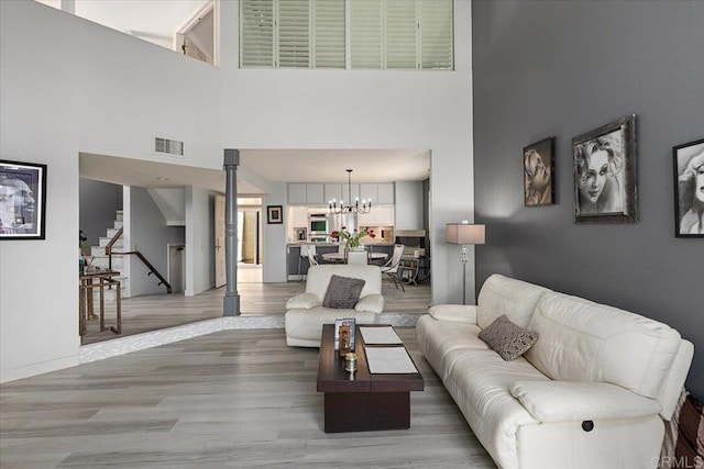 living room with visible vents, stairs, a high ceiling, light wood finished floors, and a notable chandelier