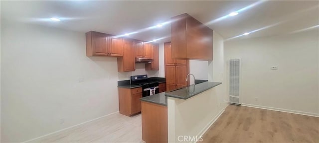 kitchen with dark countertops, gas range, a peninsula, baseboards, and light wood-type flooring