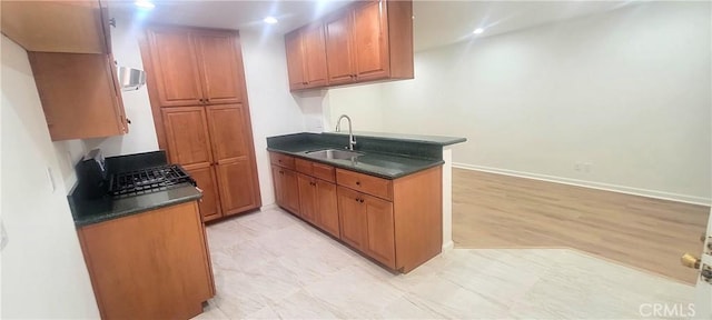kitchen featuring a sink, dark countertops, brown cabinetry, and a peninsula