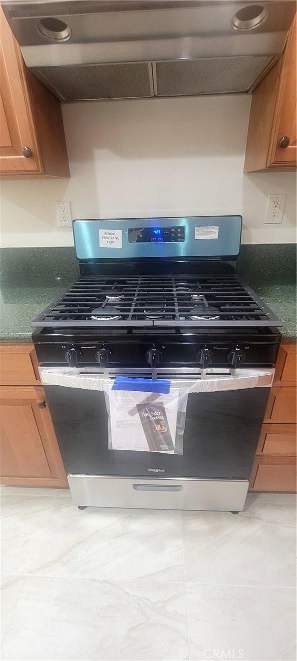 details featuring brown cabinetry, dark countertops, gas stove, and range hood