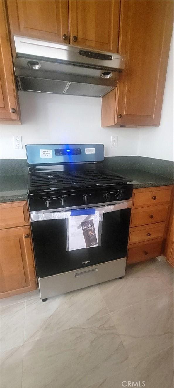 interior details featuring stainless steel range with gas cooktop, dark countertops, under cabinet range hood, and brown cabinetry