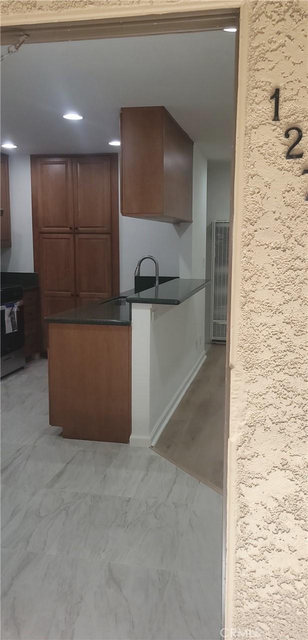 kitchen featuring dark countertops, a sink, a peninsula, marble finish floor, and recessed lighting
