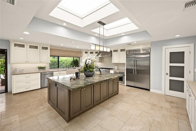 kitchen with a raised ceiling, stainless steel appliances, tasteful backsplash, under cabinet range hood, and a skylight