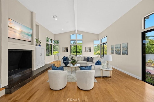 living room featuring a healthy amount of sunlight, vaulted ceiling with beams, a fireplace, and wood finished floors