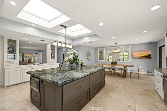 kitchen featuring a skylight, glass insert cabinets, white cabinets, and stone tile floors