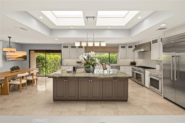 kitchen featuring white cabinetry, a skylight, range hood, and high quality appliances