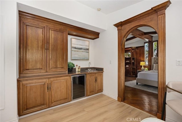 bar with a sink, baseboards, indoor wet bar, wine cooler, and light wood-style flooring