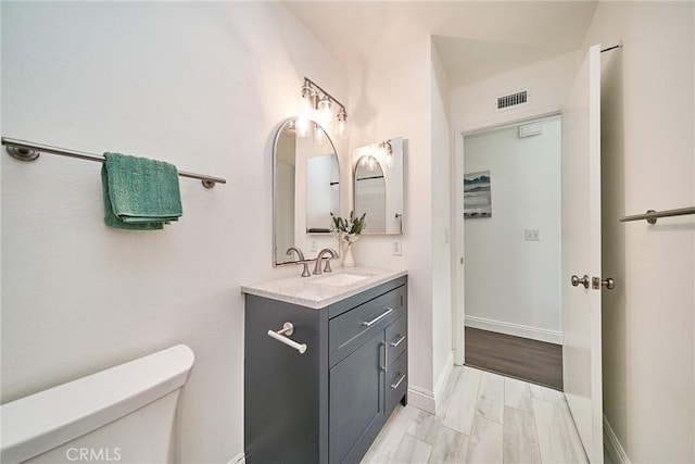 half bathroom featuring toilet, baseboards, visible vents, and vanity