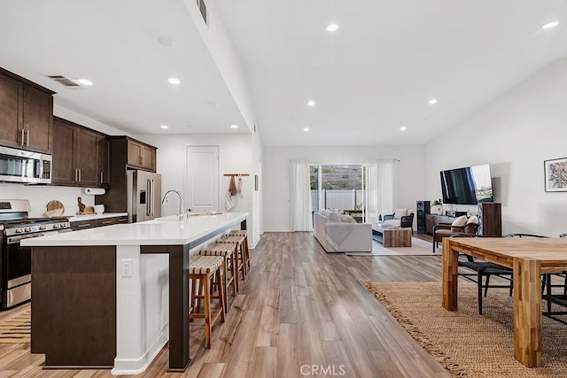 kitchen featuring dark brown cabinets, appliances with stainless steel finishes, a kitchen island with sink, lofted ceiling, and visible vents