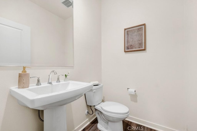 half bathroom with baseboards, wood finished floors, visible vents, and toilet