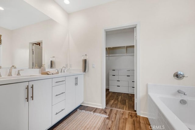 full bathroom featuring double vanity, a sink, wood finished floors, and a washtub