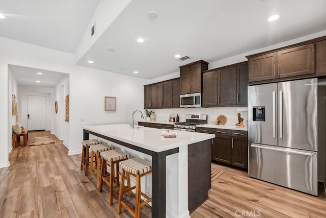kitchen with dark brown cabinetry, visible vents, appliances with stainless steel finishes, a center island with sink, and a breakfast bar