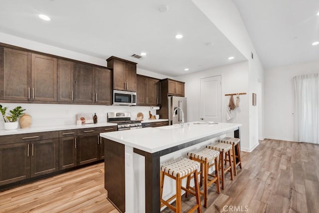 kitchen featuring a kitchen island with sink, stainless steel appliances, light wood finished floors, and a kitchen bar