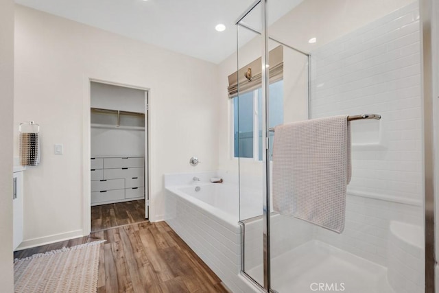 full bathroom with a walk in closet, a shower stall, wood finished floors, and a bath