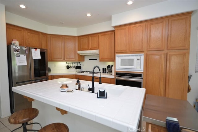 31105 Sunningdale Dr, Temecula, CA 92591 - kitchen with appliances with stainless steel finishes, a sink, a breakfast bar area, brown cabinetry, and recessed lighting