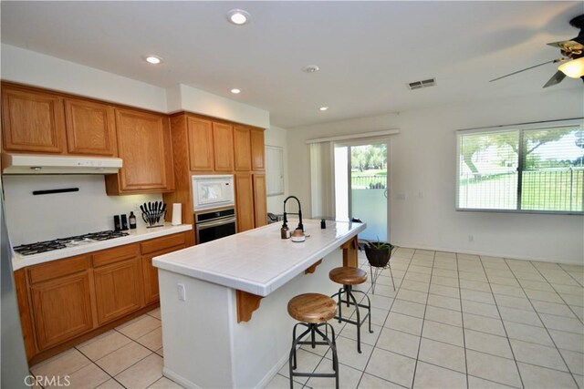 31105 Sunningdale Dr, Temecula, CA 92591 - kitchen with white appliances, under cabinet range hood, a ceiling fan, tile counters, and an island with sink