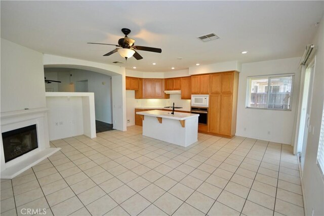 31105 Sunningdale Dr, Temecula, CA 92591 - kitchen with stainless steel oven, white microwave, ceiling fan, a fireplace with raised hearth, and an island with sink