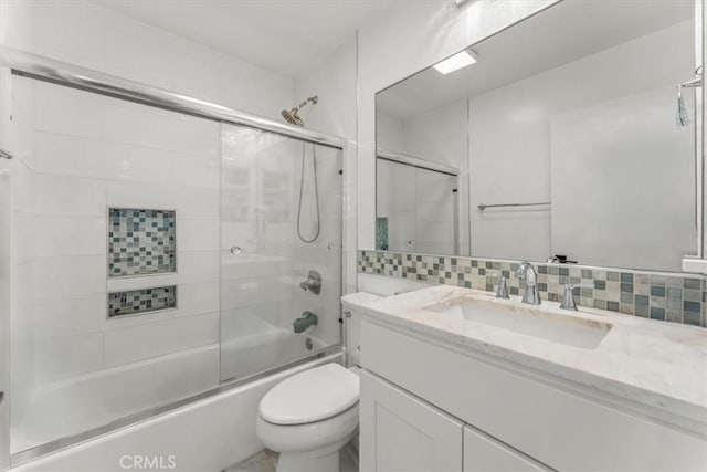 bathroom with vanity, decorative backsplash, toilet, and shower / bath combination with glass door