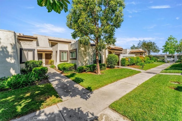 view of property featuring stucco siding, a tile roof, and a front lawn