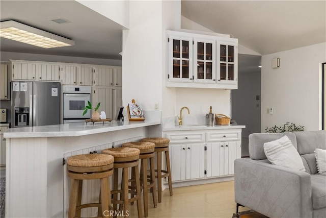 kitchen featuring a peninsula, glass insert cabinets, stainless steel fridge, light countertops, and vaulted ceiling