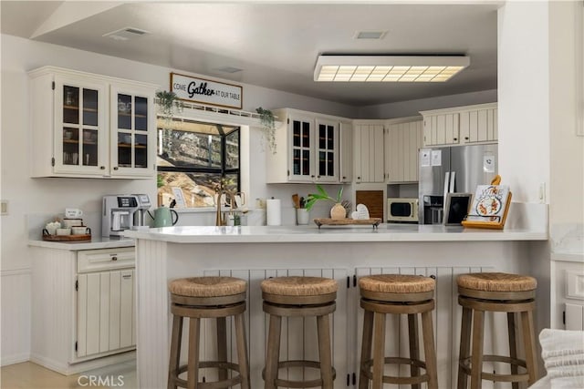 kitchen with white microwave, a peninsula, stainless steel fridge with ice dispenser, and light countertops