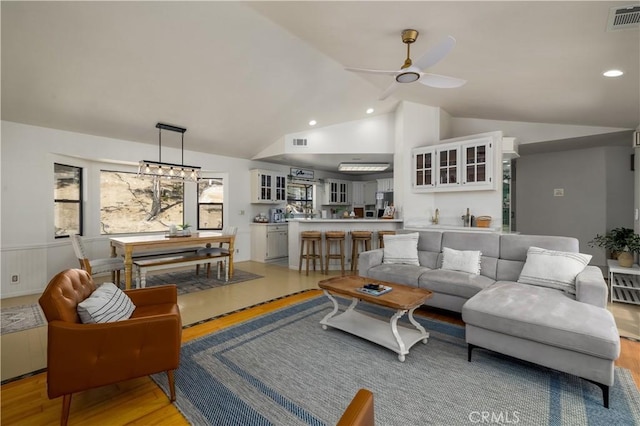 living area with vaulted ceiling, light wood-style floors, visible vents, and ceiling fan