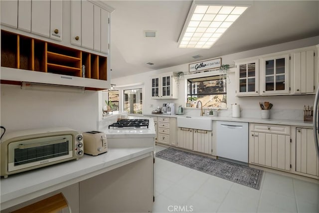 kitchen featuring a toaster, glass insert cabinets, dishwasher, a sink, and light countertops