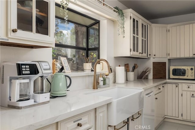 kitchen with white microwave, light stone countertops, a sink, and glass insert cabinets