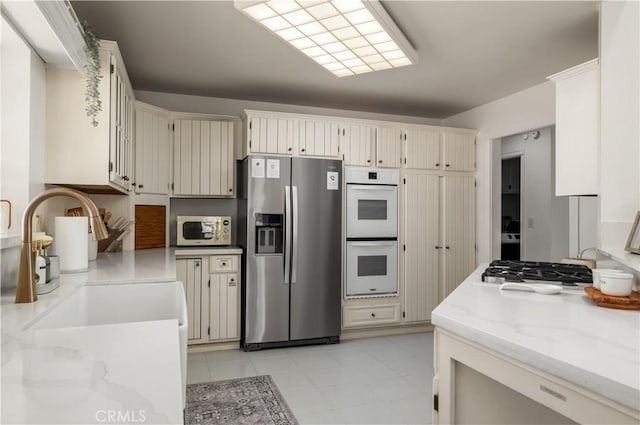 kitchen with cream cabinets, white appliances, a sink, and light stone counters