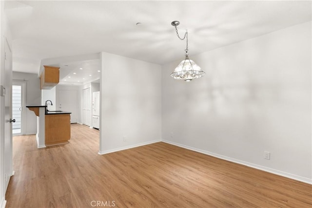 unfurnished dining area featuring baseboards, a sink, light wood finished floors, and a chandelier