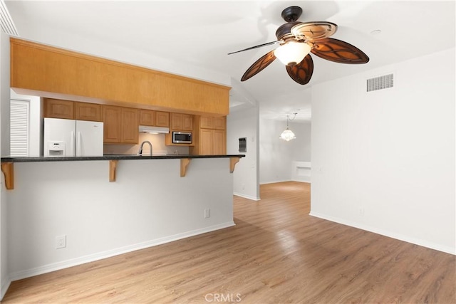 kitchen with a kitchen breakfast bar, ceiling fan, visible vents, stainless steel microwave, and white fridge with ice dispenser