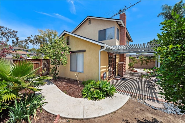 view of side of home featuring fence, a pergola, stucco siding, a chimney, and a patio area