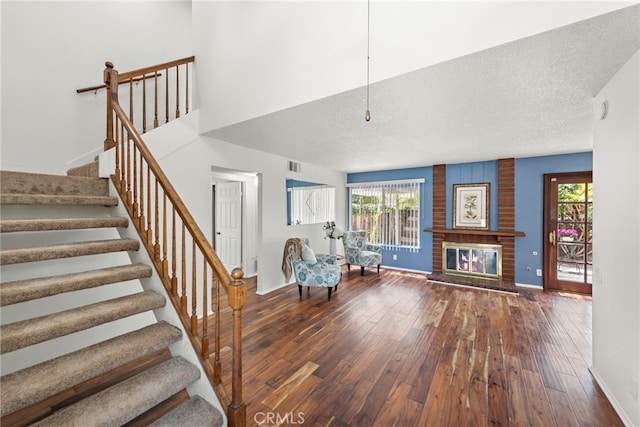 stairway with a fireplace, a textured ceiling, baseboards, visible vents, and hardwood / wood-style flooring