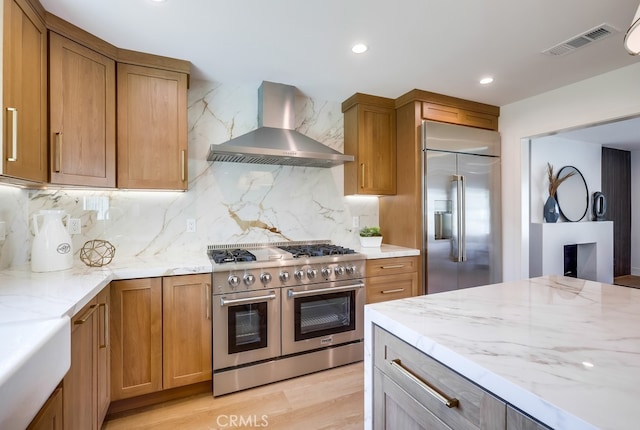 2027 Kornat Dr, Costa Mesa, CA 92626 - kitchen featuring wall chimney exhaust hood, high quality appliances, tasteful backsplash, light stone counters, and brown cabinetry