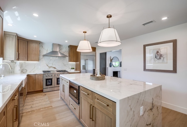 2027 Kornat Dr, Costa Mesa, CA 92626 - kitchen featuring wall chimney range hood, built in appliances, tasteful backsplash, a center island, and light stone countertops
