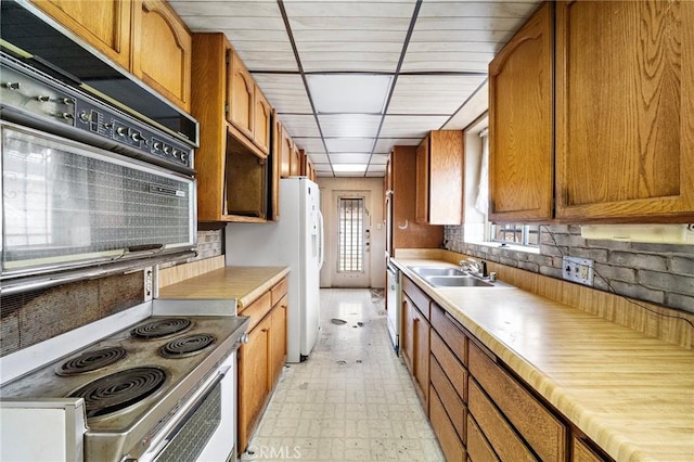 kitchen featuring brown cabinets, a sink, decorative backsplash, and range with electric stovetop