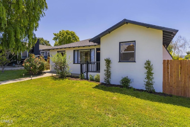 view of side of property featuring fence, stucco siding, a lawn, and a shingled roof